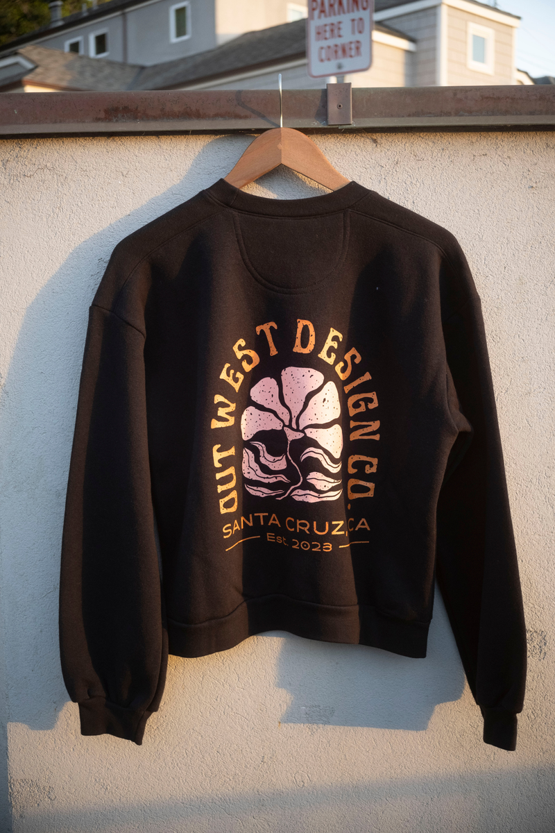 Black sweatshirt with graphic design on a hanger against a textured wall.