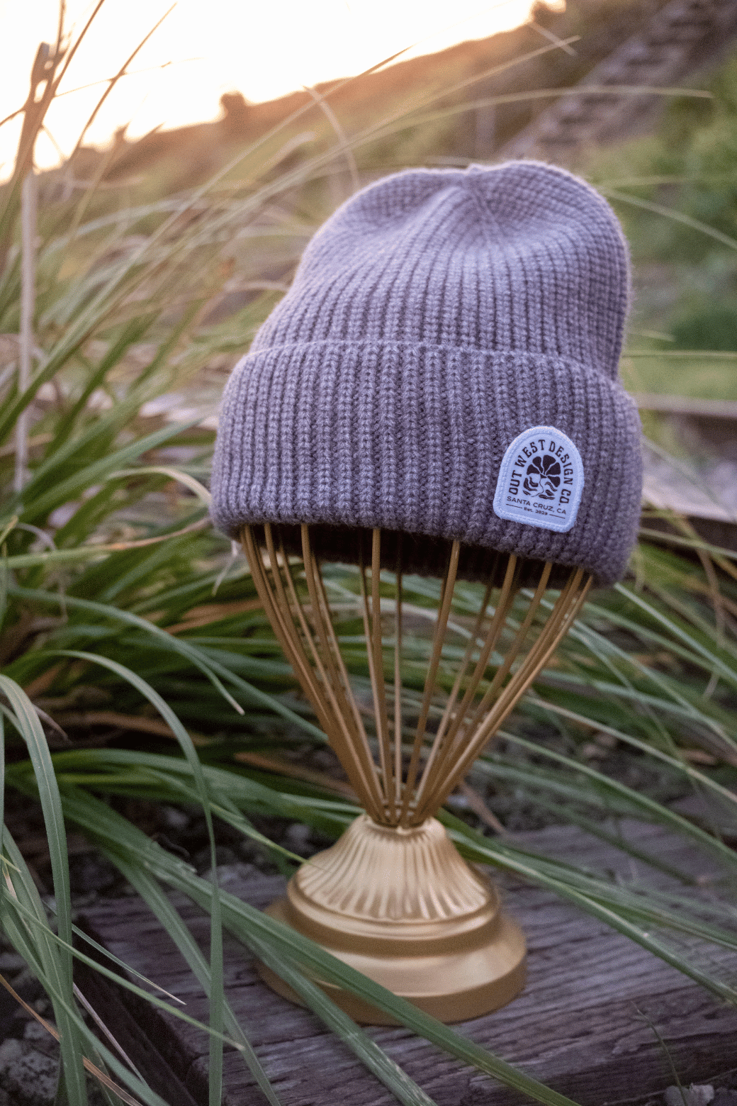 Purple knit beanie with a logo on a decorative stand against a natural background