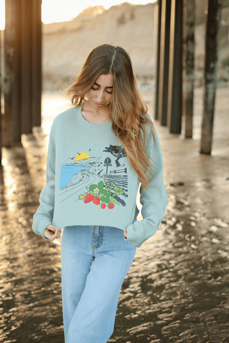 Woman wearing a light blue sweater with a graphic design, standing under a bridge.