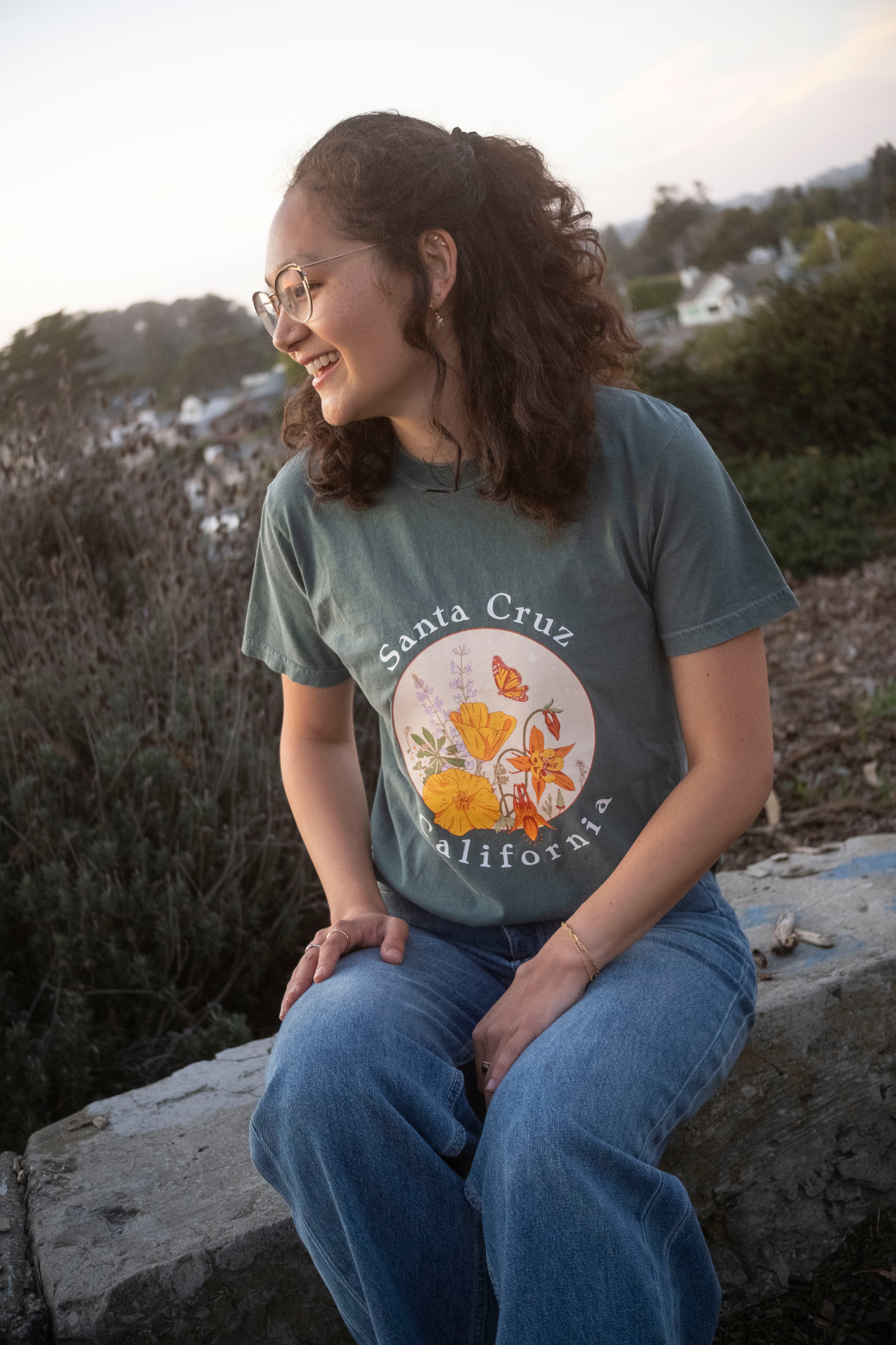 Woman wearing a 'Santa Cruz California' t-shirt with floral design, sitting outdoors.