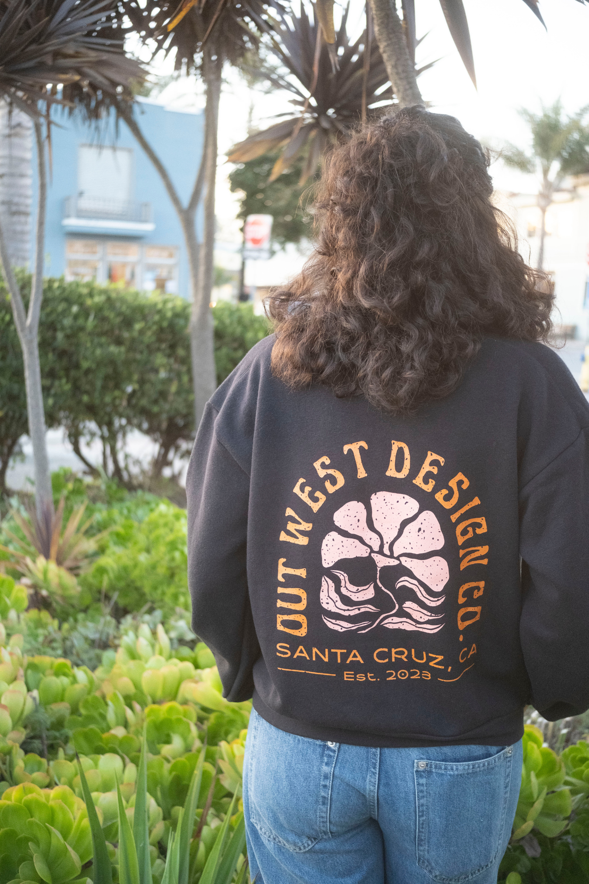 Person wearing a black sweatshirt with 'Out West Design Co' logo in an outdoor setting.