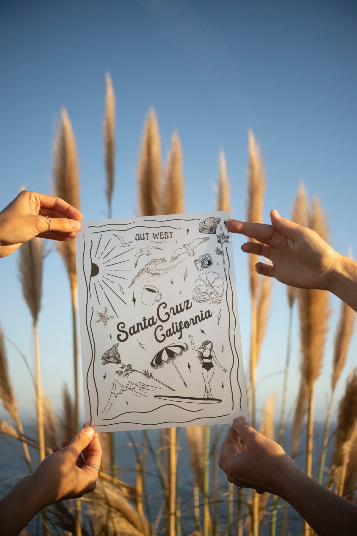 Person holding a printed map of Santa Cruz, California against a backdrop of tall grasses and blue sky.
