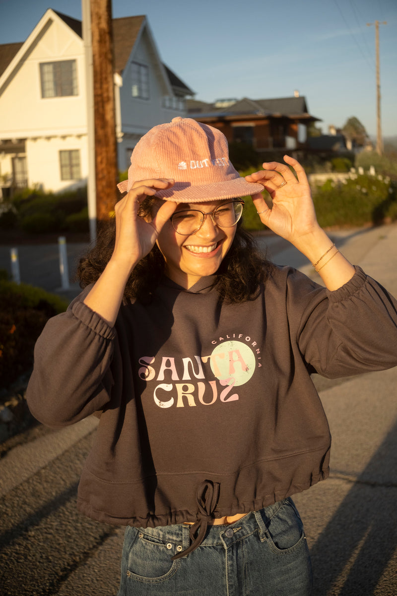 Person wearing a pink cap and Santa Cruz hoodie on a residential street.