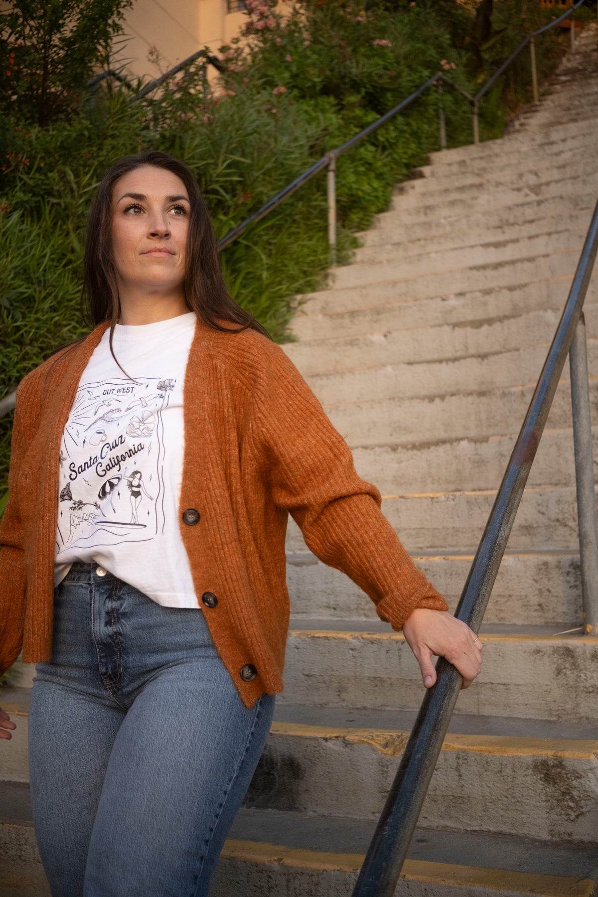 Woman in an orange cardigan and white t-shirt standing on outdoor steps.