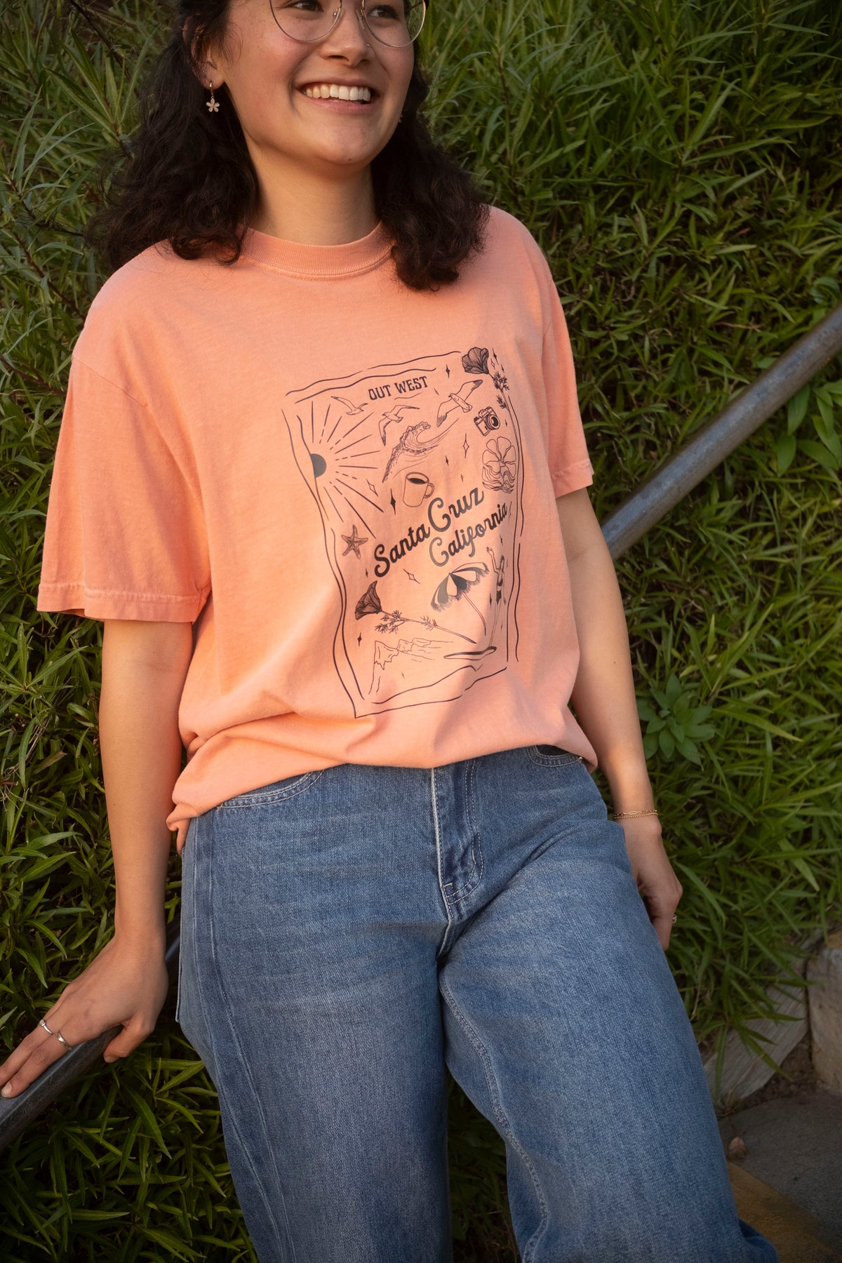 A woman wearing an orange t-shirt leans against a railing.