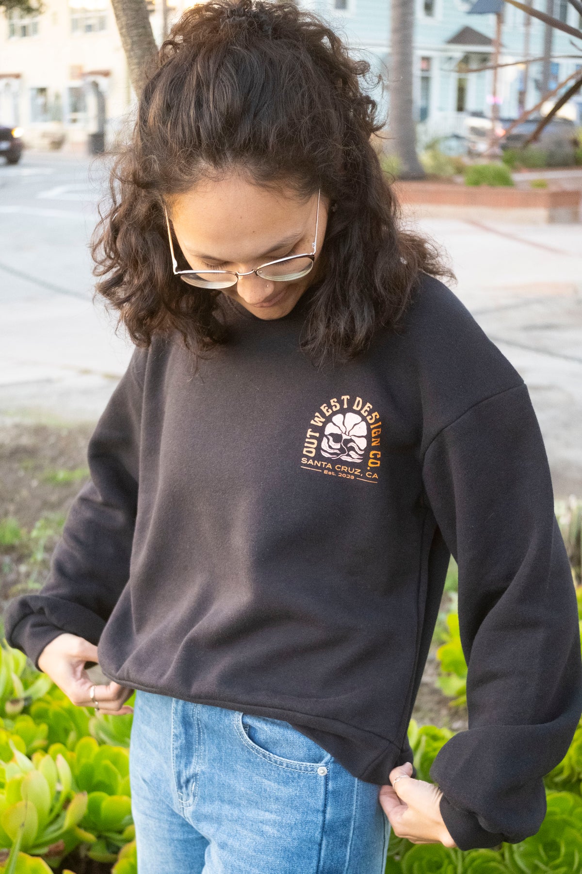 Person wearing a black sweatshirt with a logo, standing outdoors.