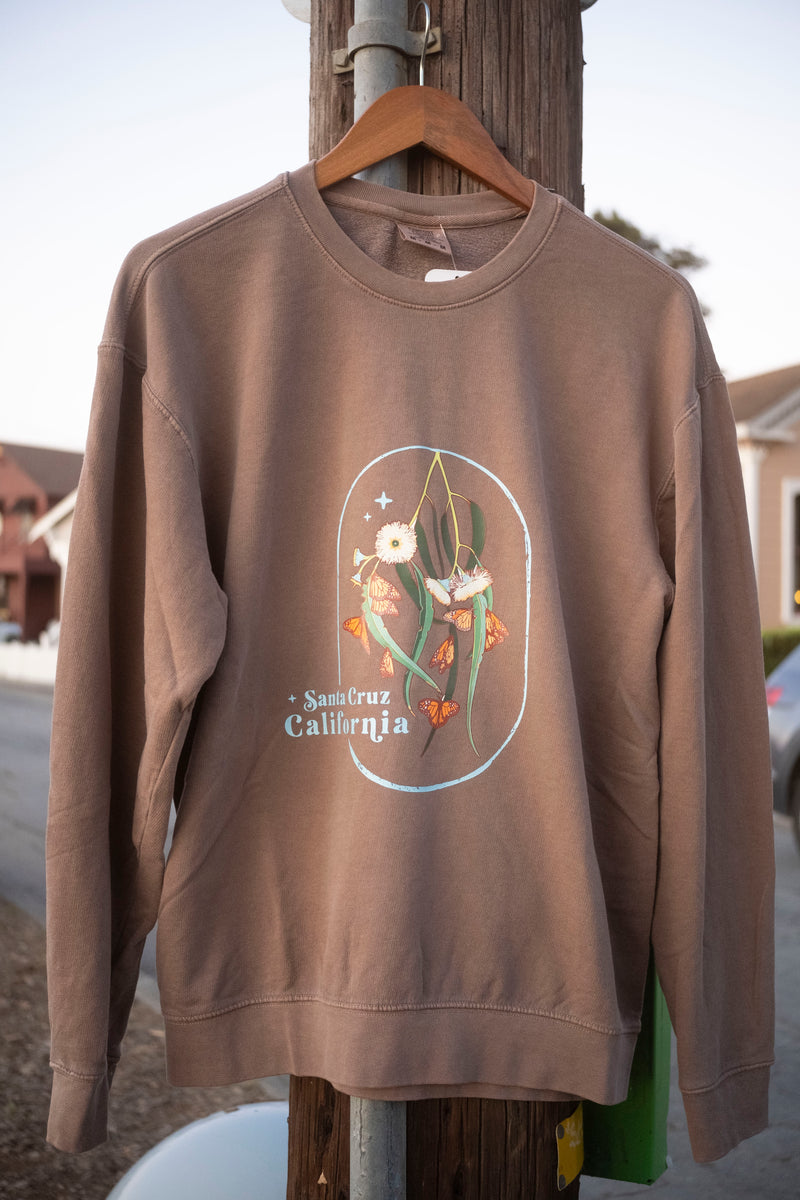 Brown sweatshirt with graphic design on a hanger against a street background
