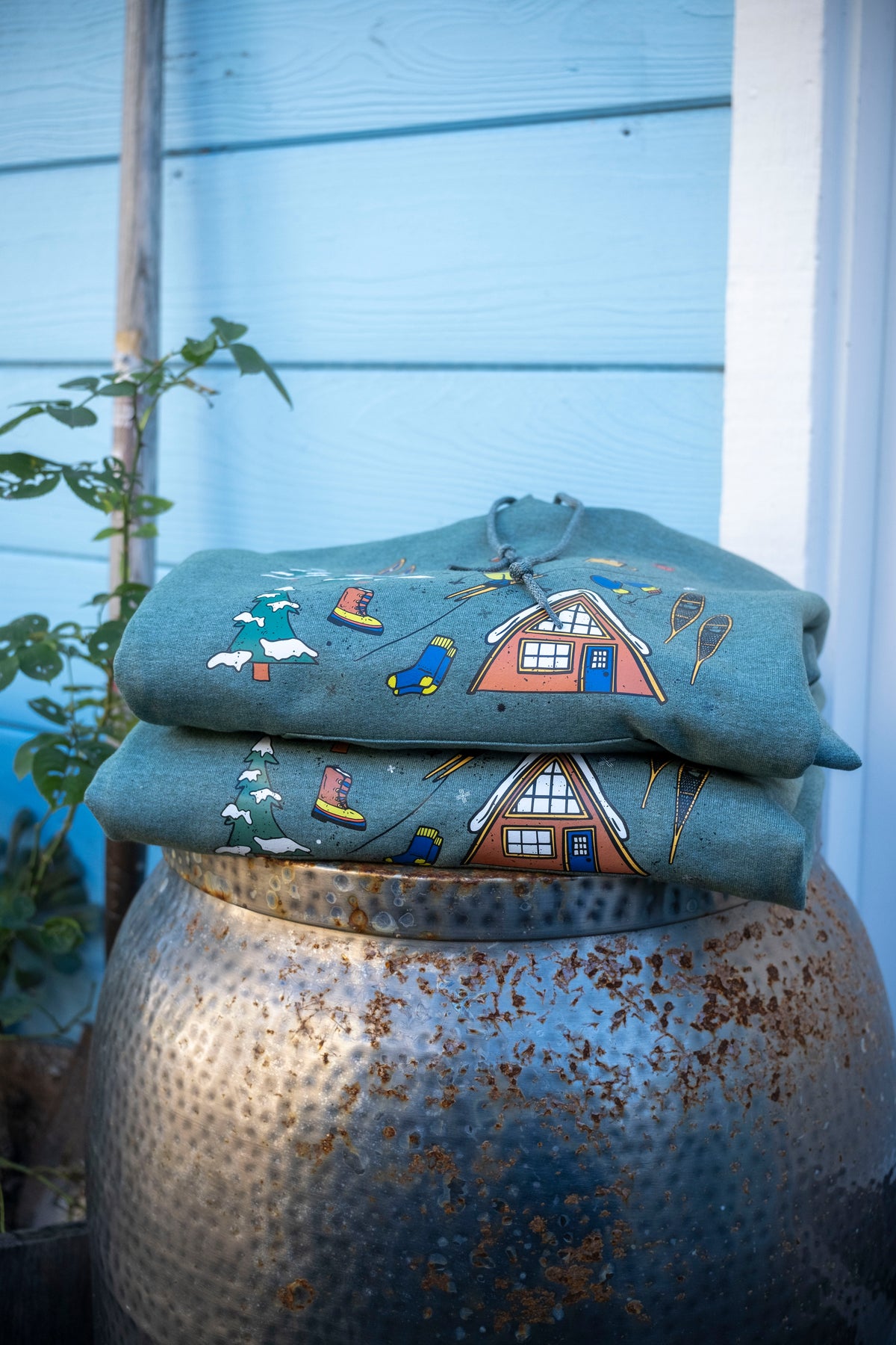 Folded fabric with house design on a rusty metal container against a light blue wall.