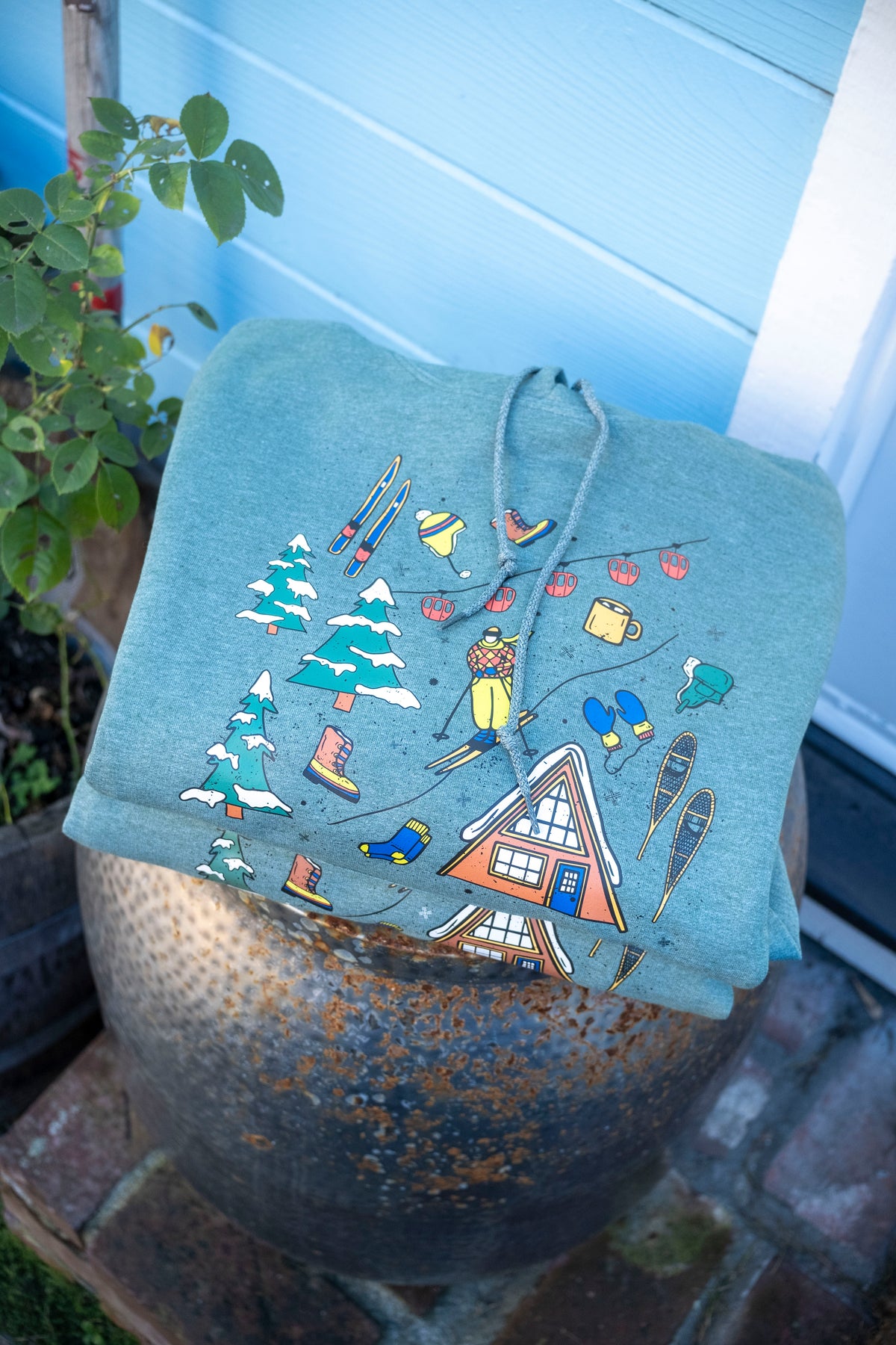 Light green hoodie with winter-themed designs on a decorative pot.