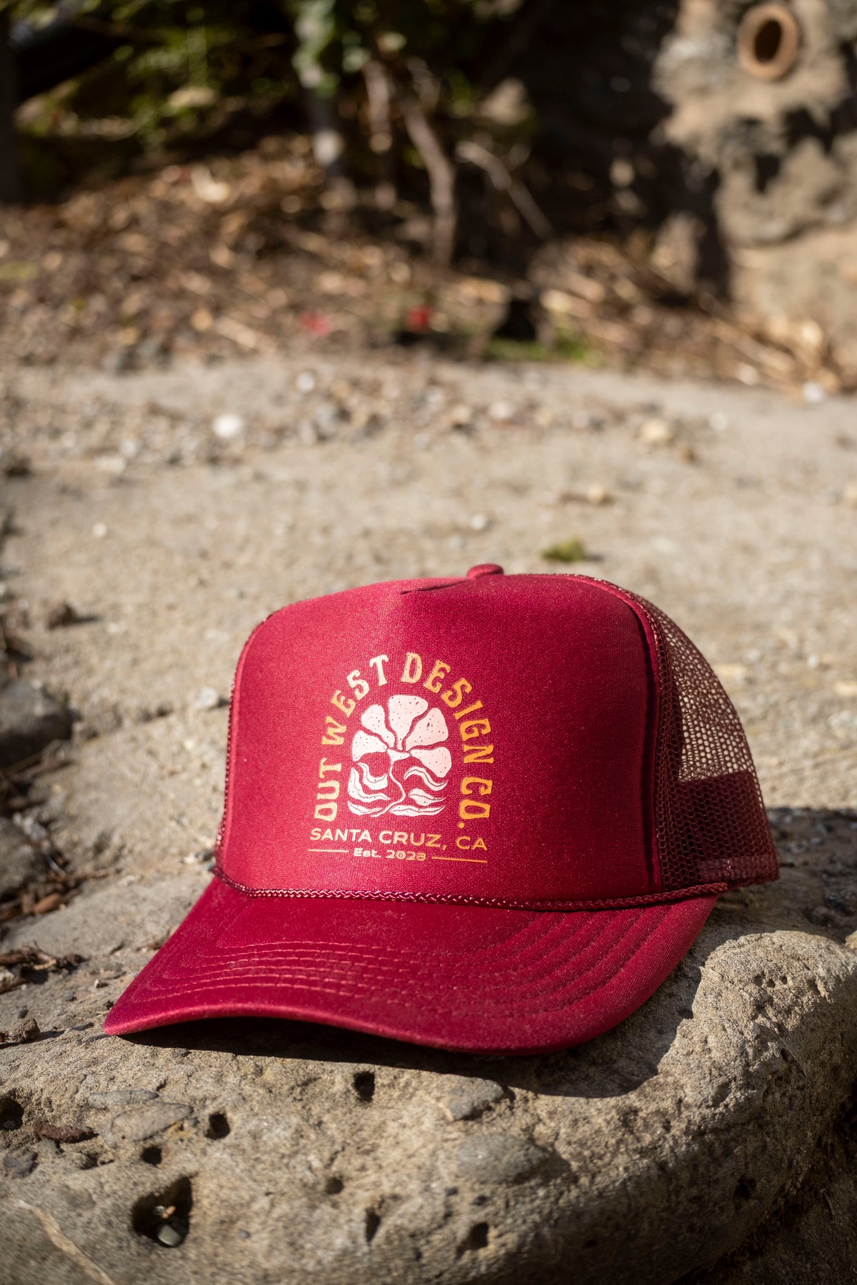 Red trucker hat with a logo and text on a stone surface