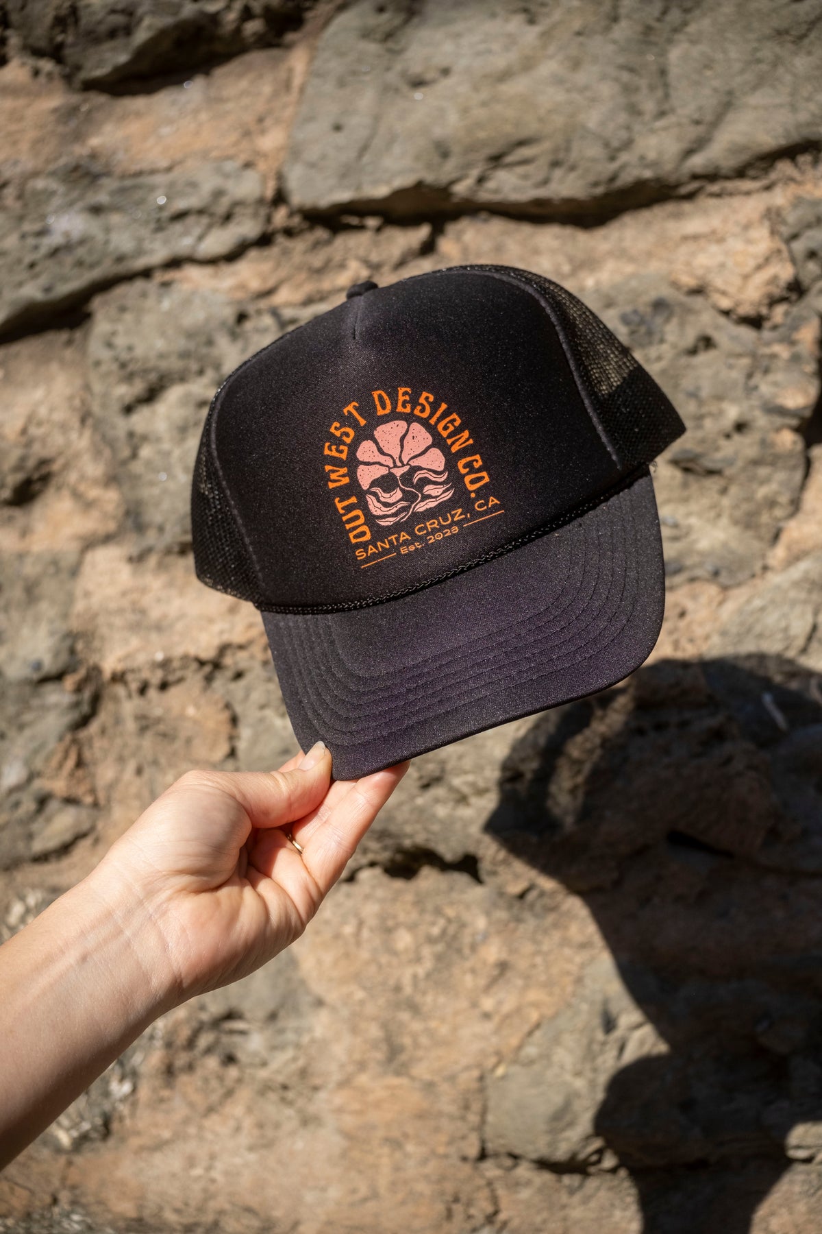 Black cap with a logo held against a stone wall
