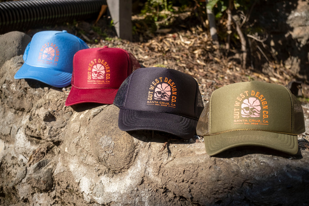 Four baseball caps in blue, red, black, and green on a stone surface with a natural background.