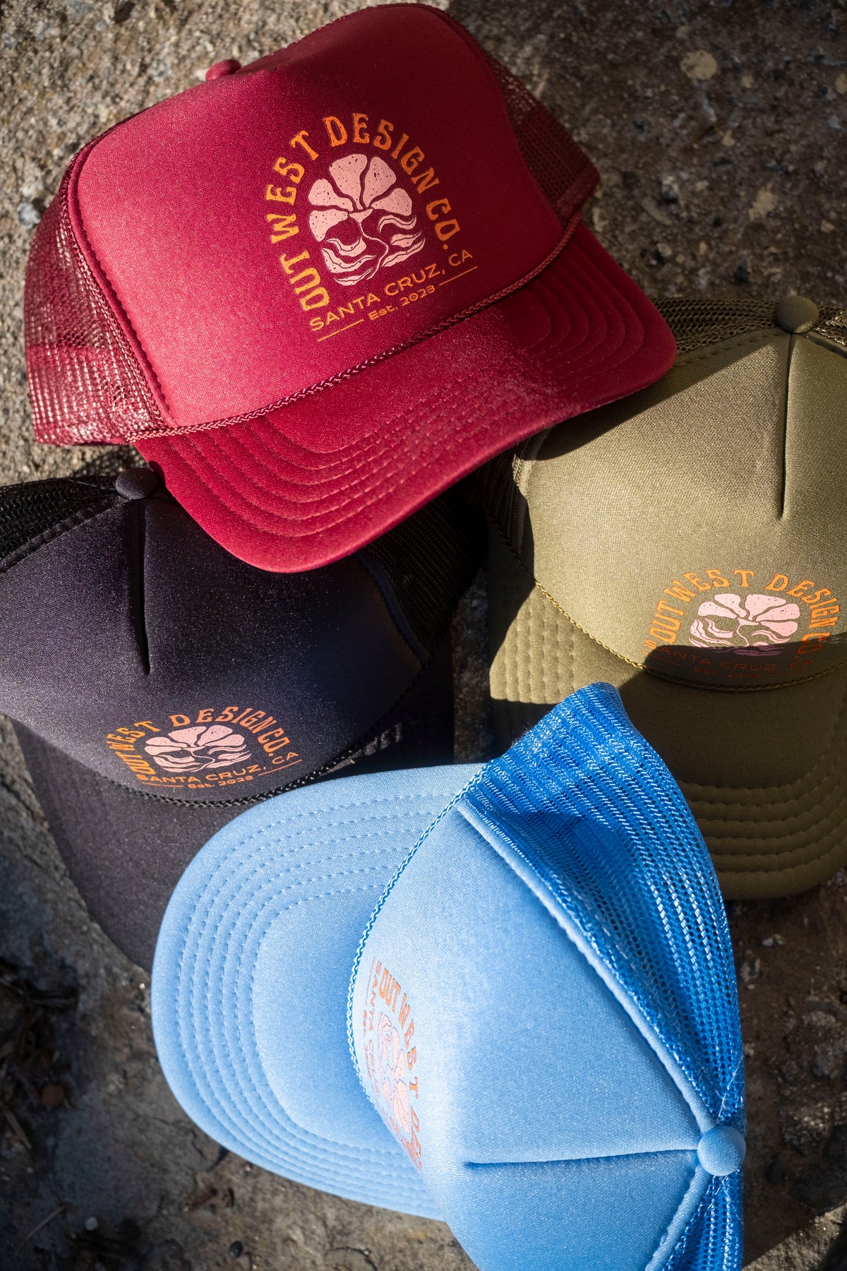 Four caps in red, black, blue, and green with a visible brand logo on a textured surface.