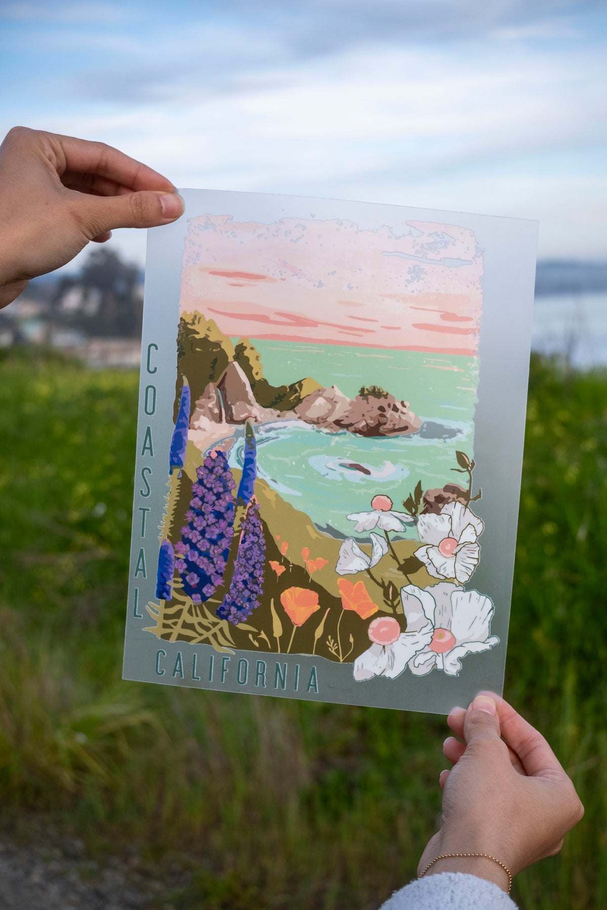 Person holding a coastal California-themed print with nature elements.