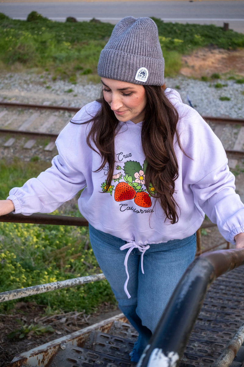 Woman wearing a white hoodie with graphics and text, standing outdoors near tracks.