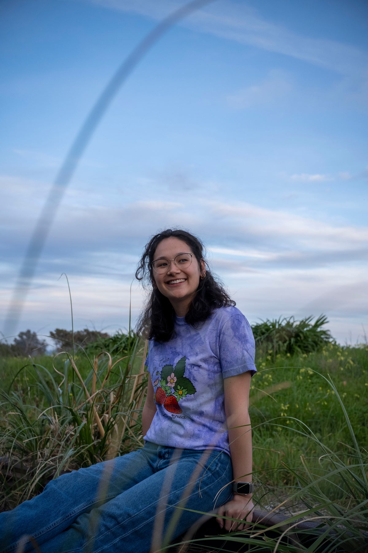 Person sitting in a grassy field with a blue sky and archway in the background