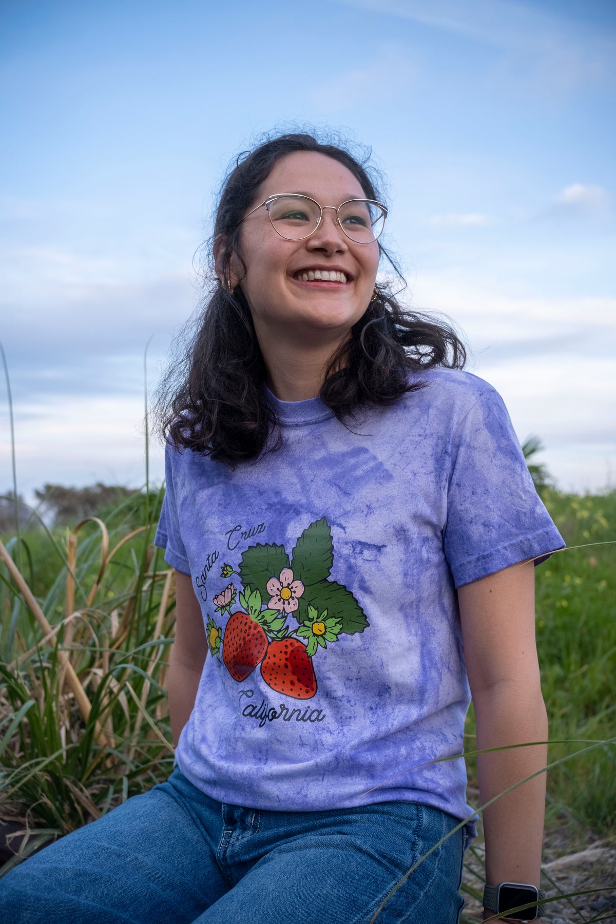 Person wearing a purple tie-dye t-shirt with a graphic design outdoors