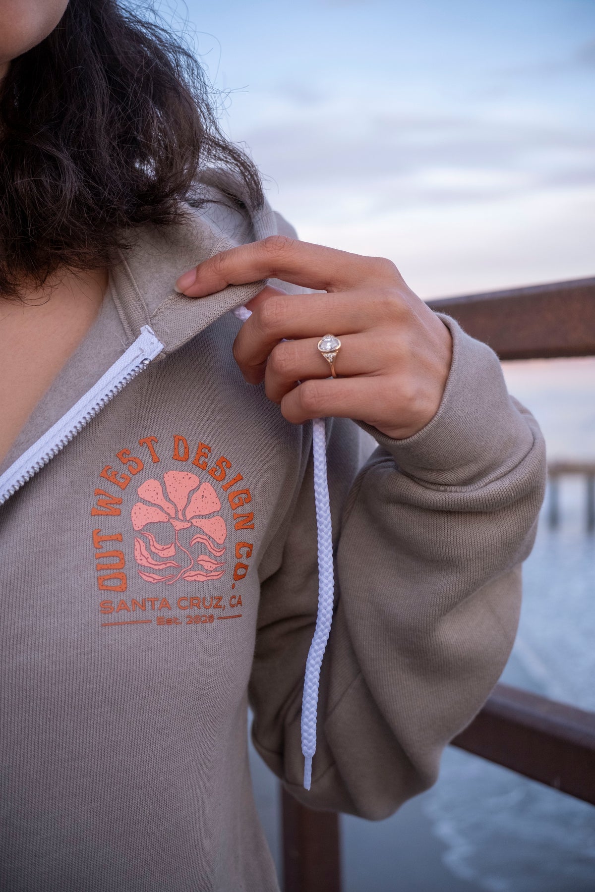 Person wearing a hoodie with a logo and text, holding the hood with a blurred background.