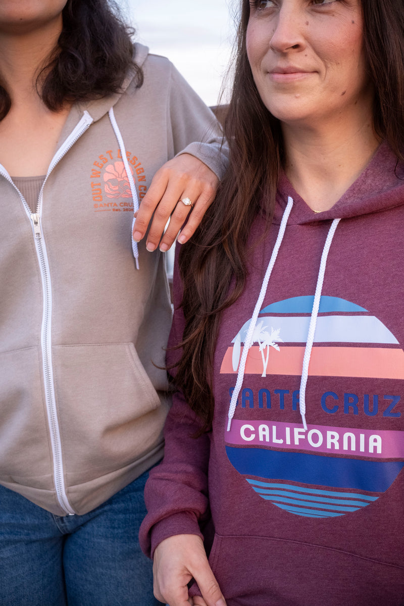 Two people wearing hoodies with visible branding, one in a beige hoodie and the other in a maroon hoodie with 'Santa Cruz California' design.