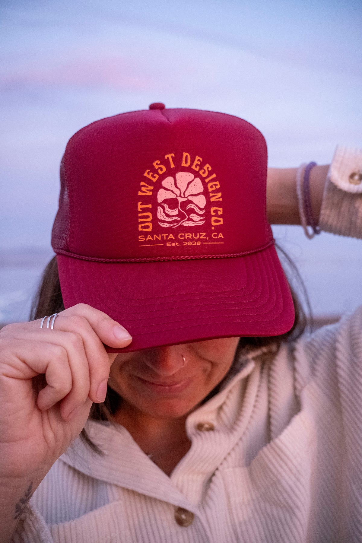 Person wearing a red cap with a logo and text, against a blurred natural background