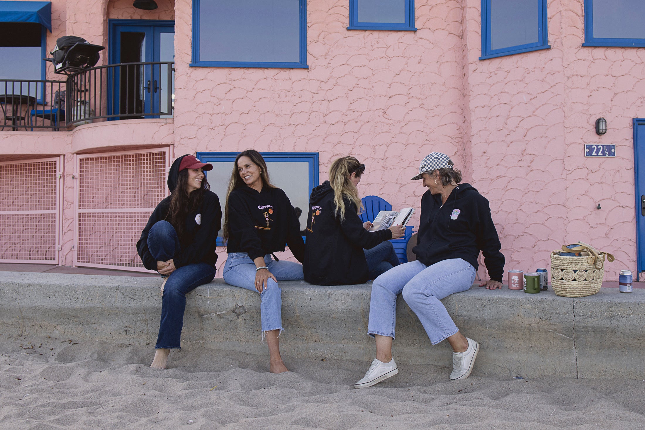 Four women sitting on a set of stairs in front of a pink building with blue accents.
