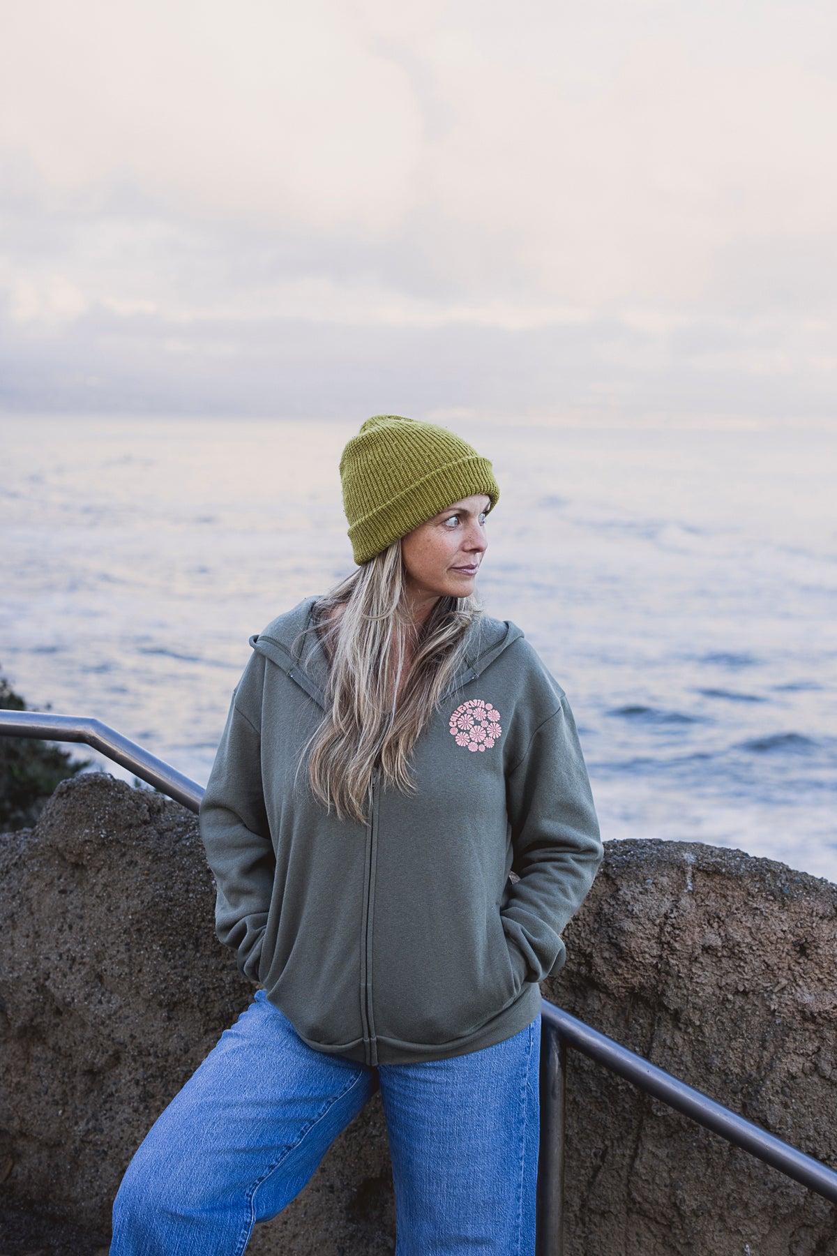 Person wearing a green beanie and jacket by the ocean