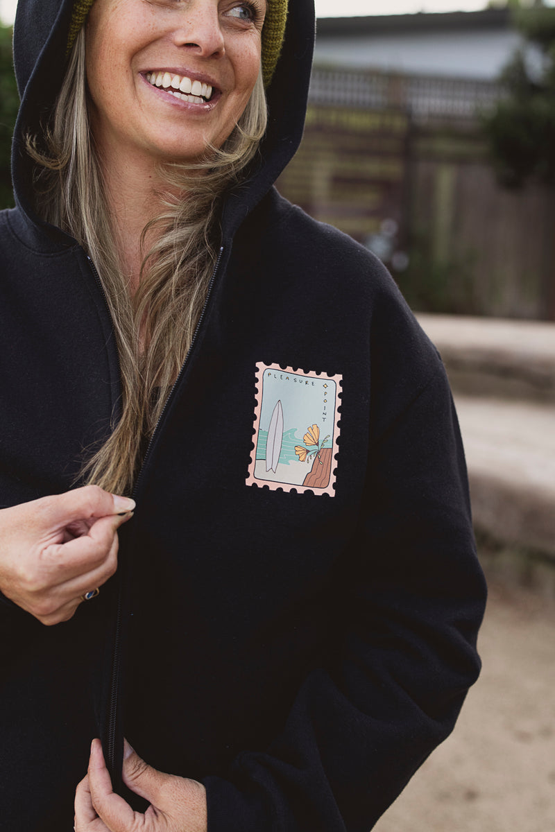 Person wearing a black hoodie with a patch on the chest, standing outdoors.