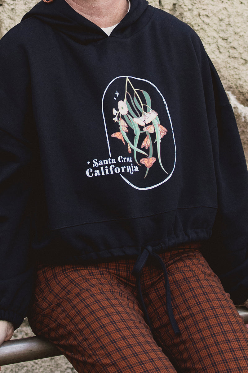 Person wearing a black hoodie with a floral design and 'Santa Cruz California' text.