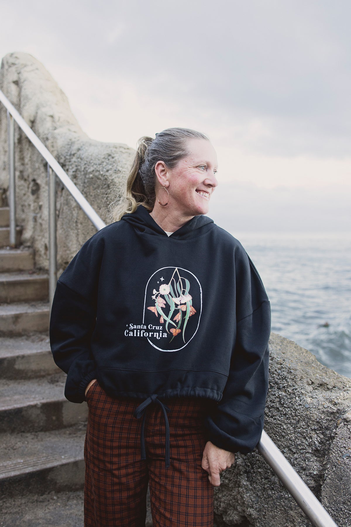 Person wearing a black hoodie with a graphic design by the sea