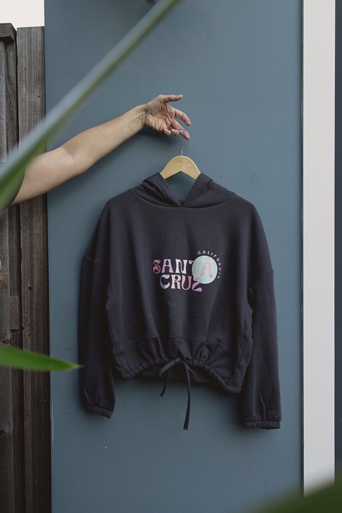 Black hoodie with 'Santa Cruz' branding on a hanger against a gray wall.