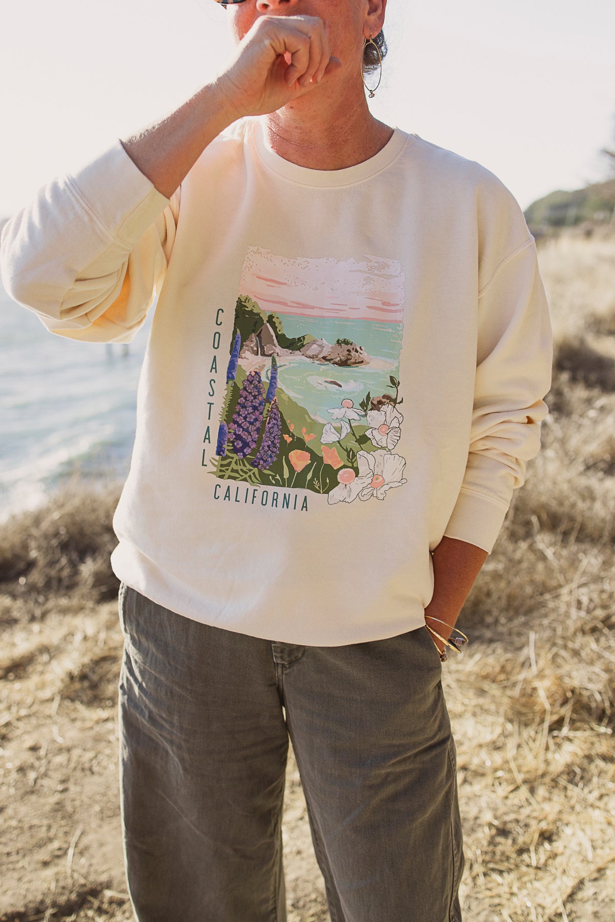 Person wearing a white sweatshirt with a scenic graphic in a natural setting
