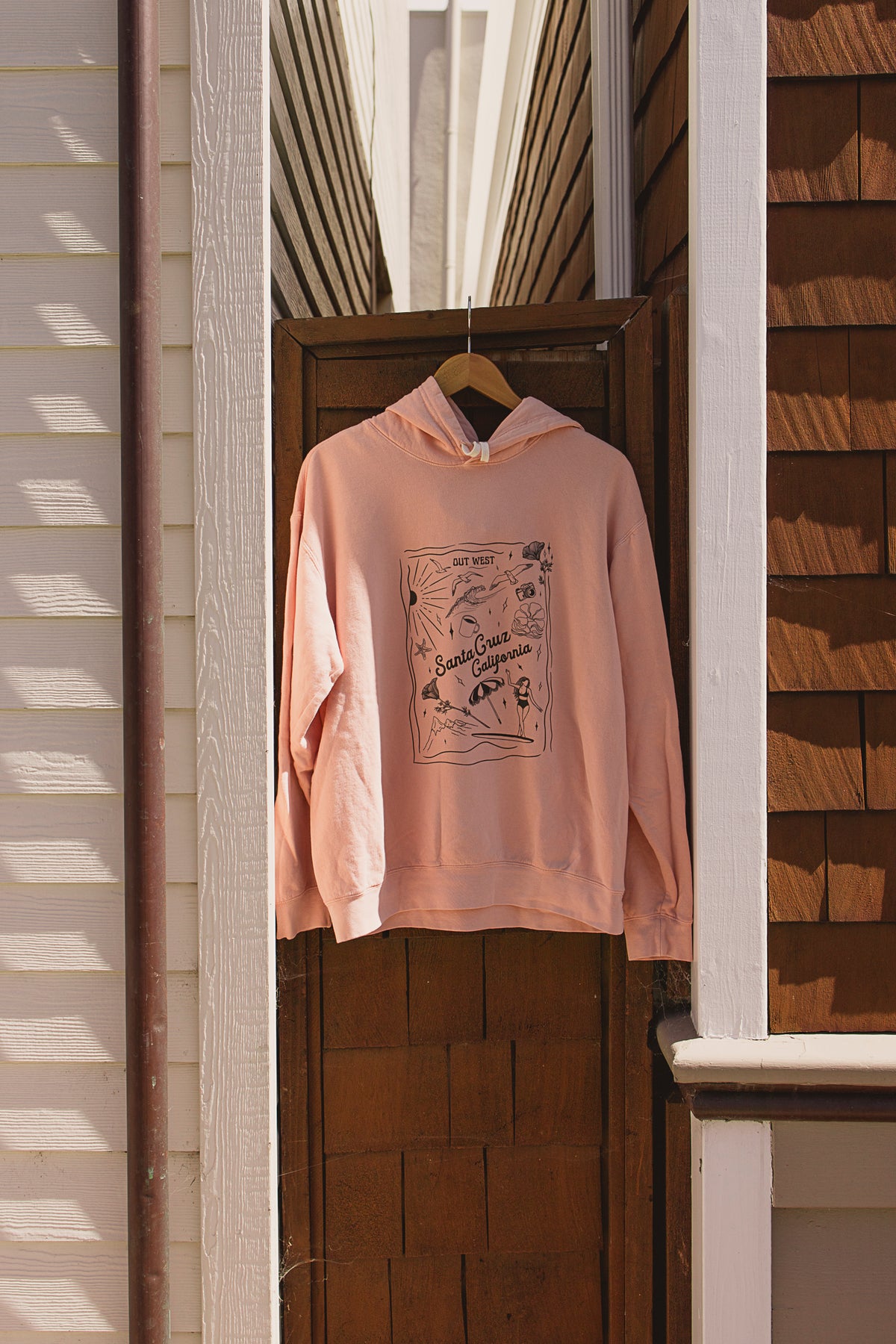 Pink hoodie with graphic design hanging on a door