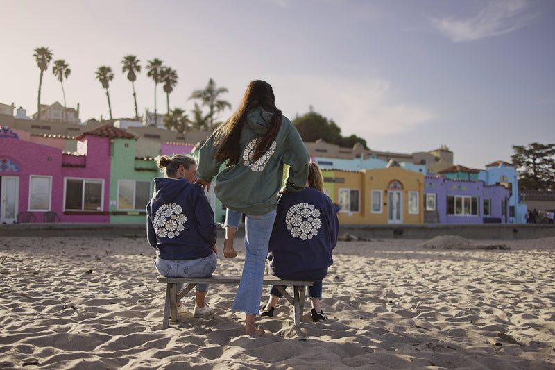 Three people sitting on a bench at the beach with colorful buildings in the background